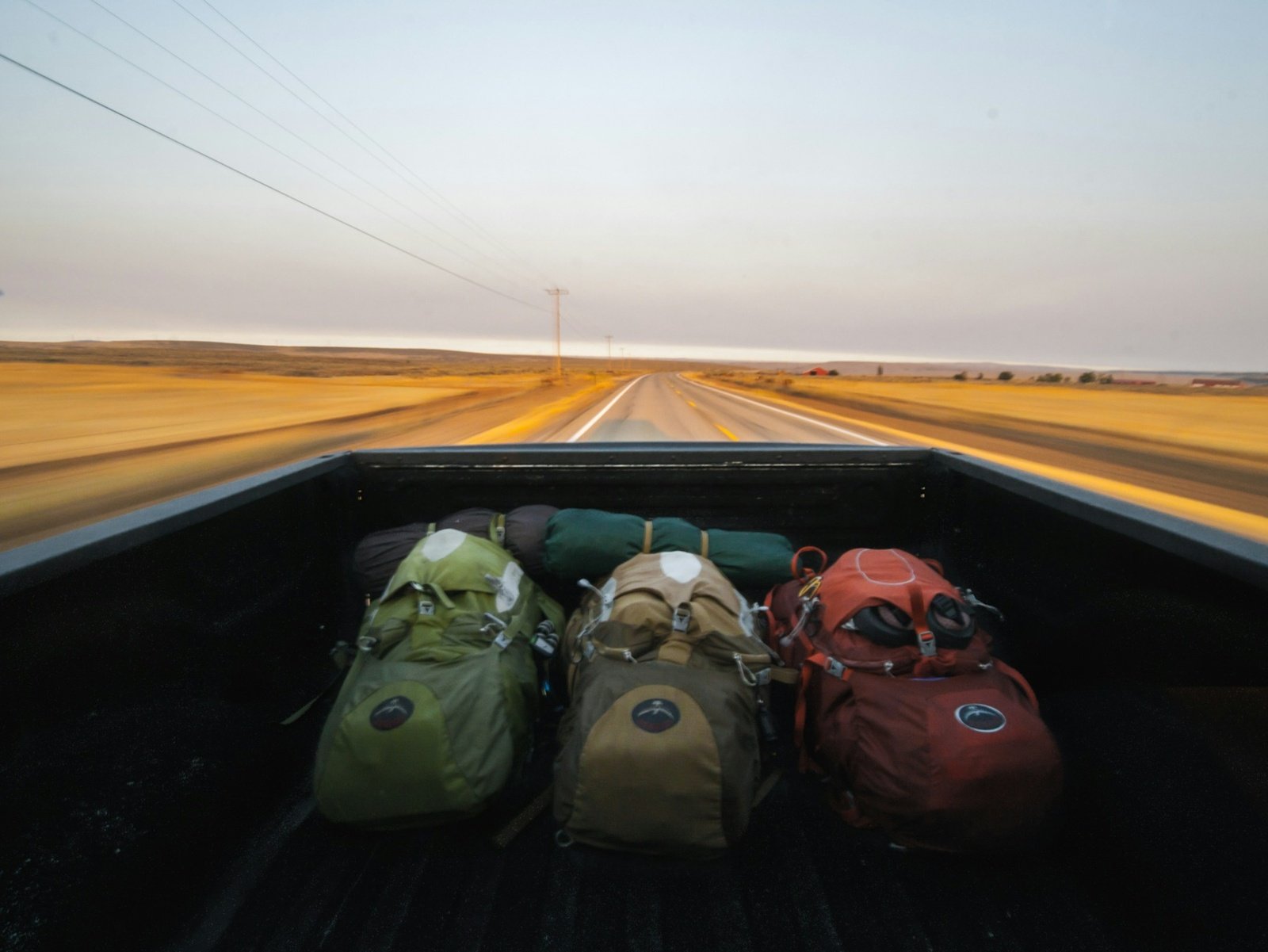 Backpacks loaded into the bed of a pickup truck on an open highway, a common sight for hitchhikers and ride-share travelers